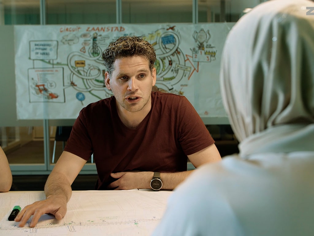 Twee Gemeente Zaanstad medewerkers in gesprek aan tafel met plattegronden, op de achtergrond een tekening van Circuit Zaanstad, employer branding video Mondha Media