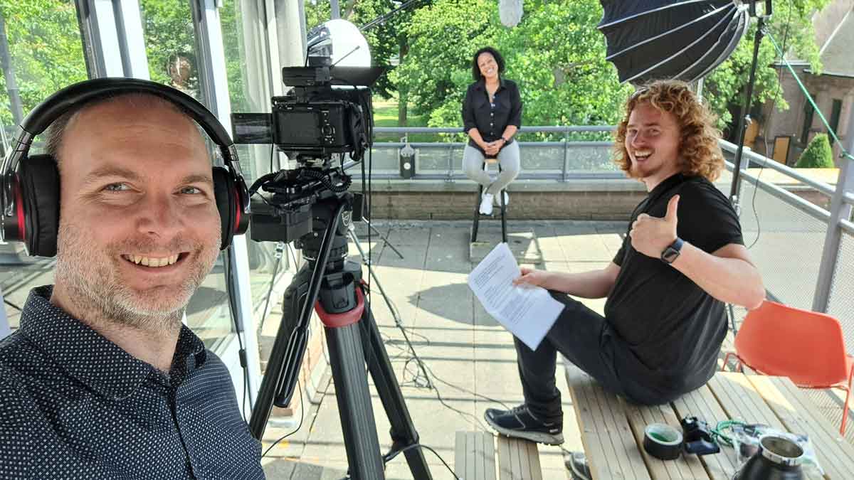 Sebastiaan van Hamond met koptelefoon en cameraman Tim geven duim omhoog voor de camera, medewerker van Parnassia LIB zit klaar voor interview op dakterras, behind the scenes recruitment campagne