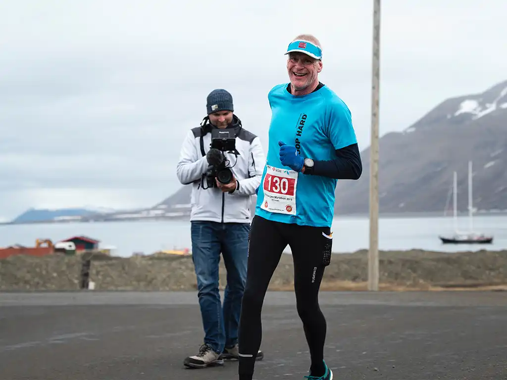 Aftermovie Arctic Marathon — loper in beeld bij de finish Lachende marathonloper met startnummer 130 wordt gefilmd door de cameraman van Mondha Media tijdens de Arctic Marathon op Spitsbergen