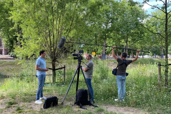 Behind the scenes interview techniek – gemeente Utrecht Filmcrew met camera en hengel neemt een interview op met een medewerker in een groene omgeving voor de wervingsvideo techniek van gemeente Utrecht