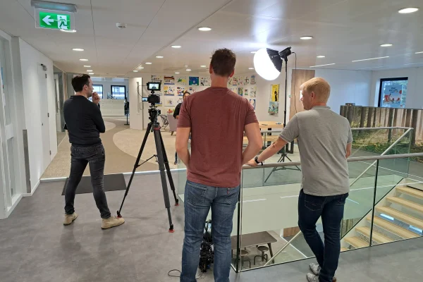 Achter de schermen bij de Haagse Hof videoproductie De filmcrew van Mondha Media voert een videoproductie uit met een camera op statief en studiobelichting in een modern kantoorpand voor de Haagse Hof interactieve film.