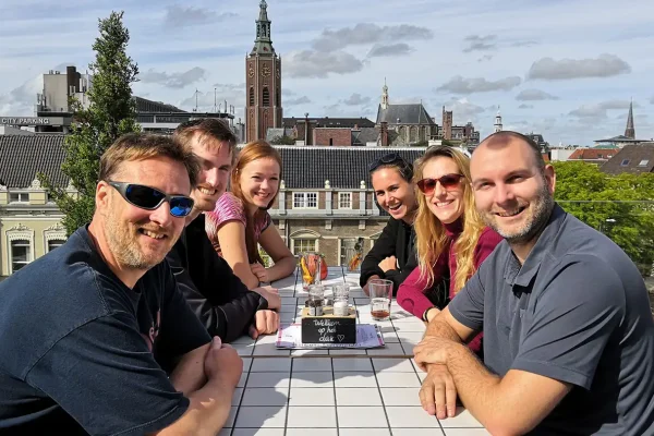 Moodfilm Hoge Vrijheid — team en figuranten op het dak Het team van Mondha Media en figuranten aan tafel op een dakterras met de skyline van Den Haag op de achtergrond tijdens de moodfilm Hoge Vrijheid