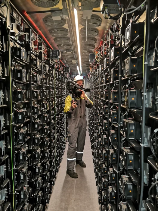 Een cameraman met een helm en professionele videocamera filmt tussen lange rijen servers en hybride batterijen voor de Uniper projectfilm.