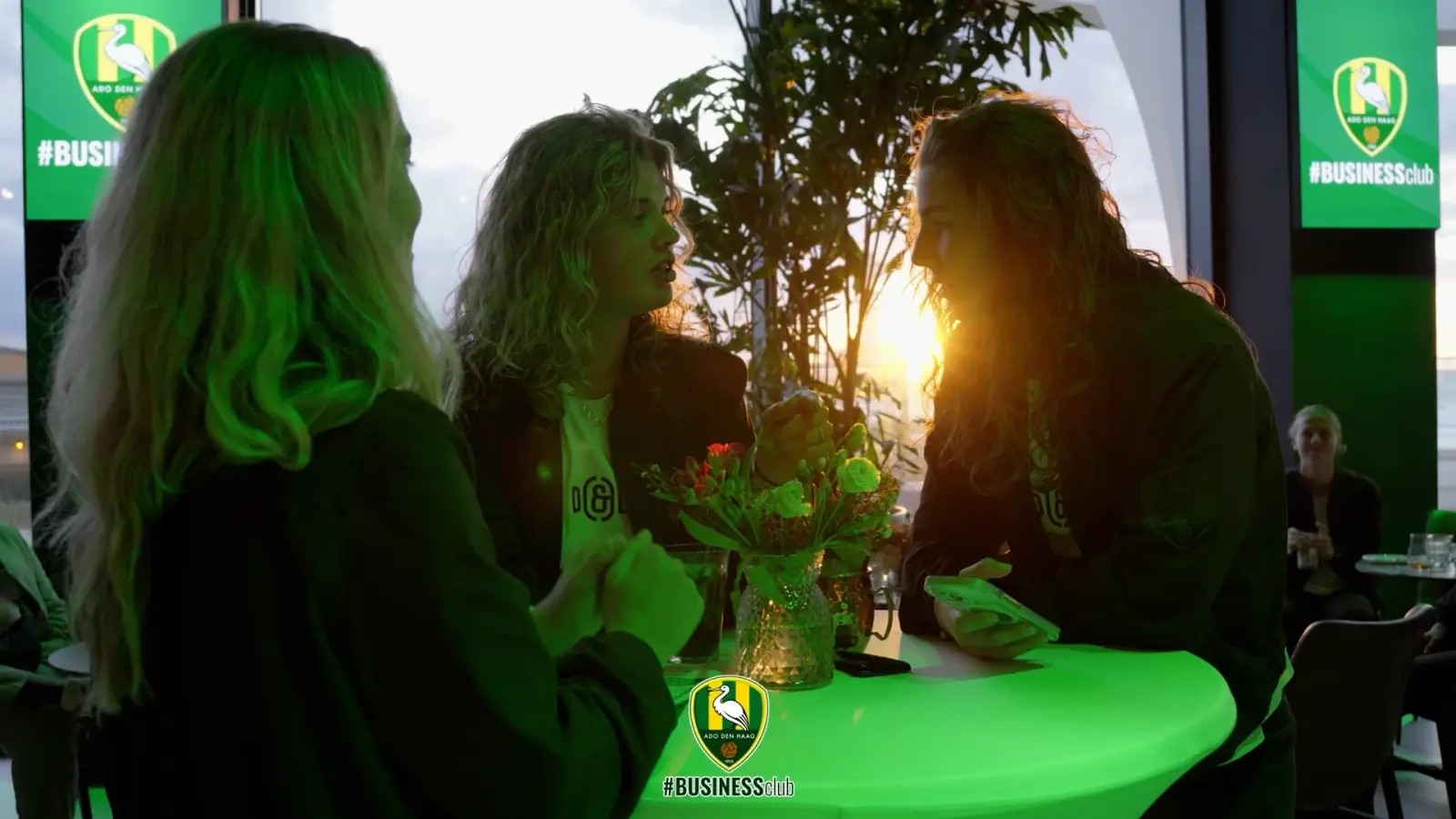 Gasten in gesprek aan een statafel bij zonsondergang tijdens de seizoensopening van de ADO Den Haag Business Club